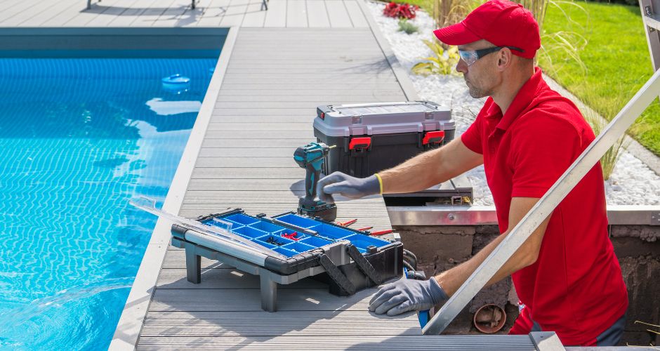 Outdoor pool maintenance worker with a toolbox and electric drill in front of him.