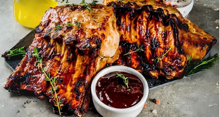 Grilled ribs with savory sauce and aromatic herbs, served on a sleek black tray.