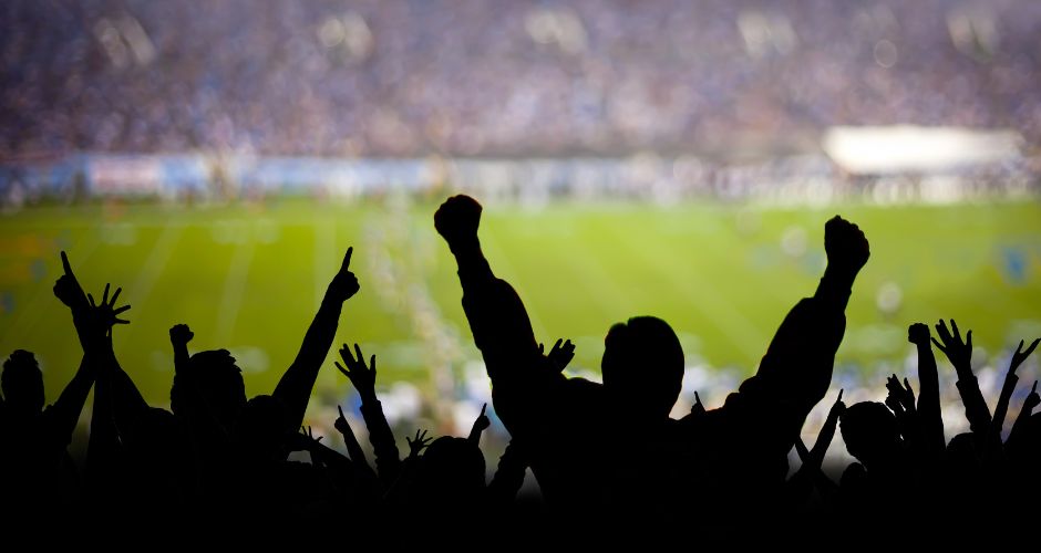 Silhouettes of cheering fans at a football game, with their arms raised in various gestures of excitement and support.